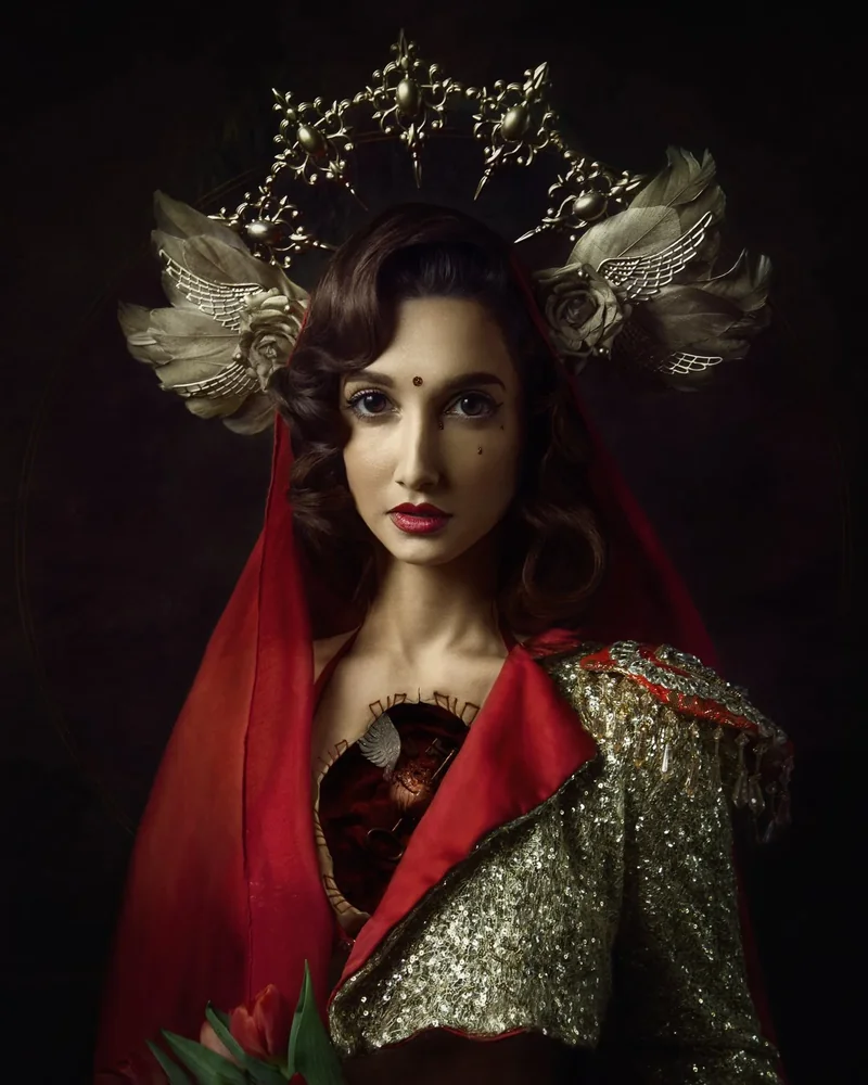 Porträt von Karolina Skorek aus der Serie Lux et Umbra: eine Frau mit rotem Schleier und einem mit Goldpailletten besetzten Umhang, mit einer vergoldeten, geflügelten Krone, vor dunklem Hintergrund