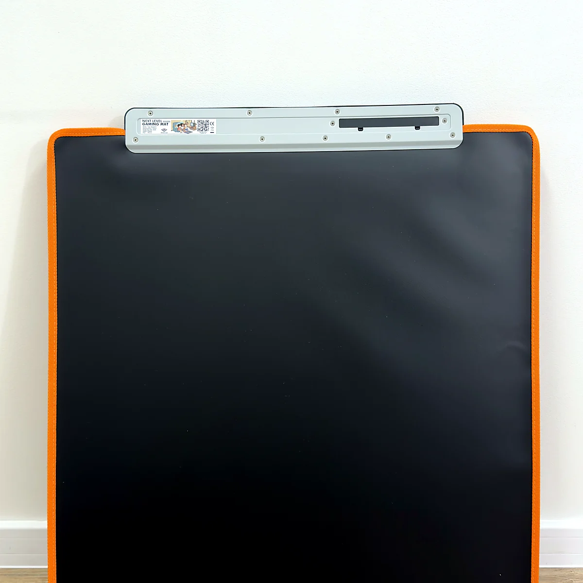 sq-nlgm-folded-upright-storage - Interactive Mats L-TEK L-TEK Next Level Gaming Mat folded flat and standing upright against a wall with its orange edge visible