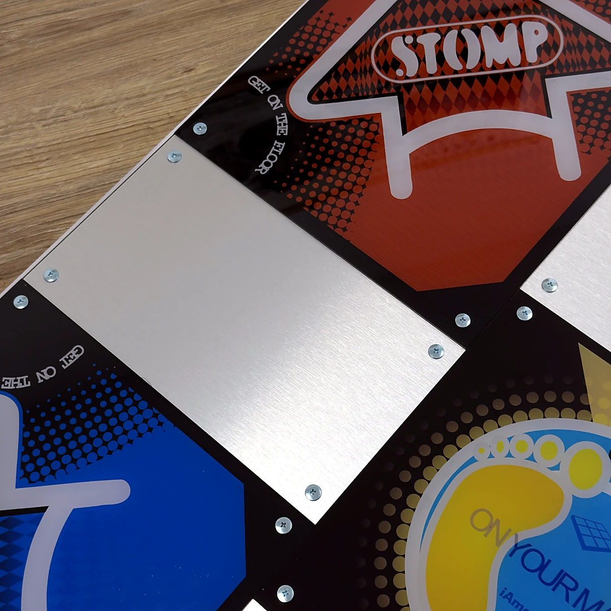 sq-piu-angled-panels - Interactive Mats L-TEK Angled view of the L-TEK PIU PRO Metal dance pad showing a STOMP panel, a brushed steel panel and the bolted joints