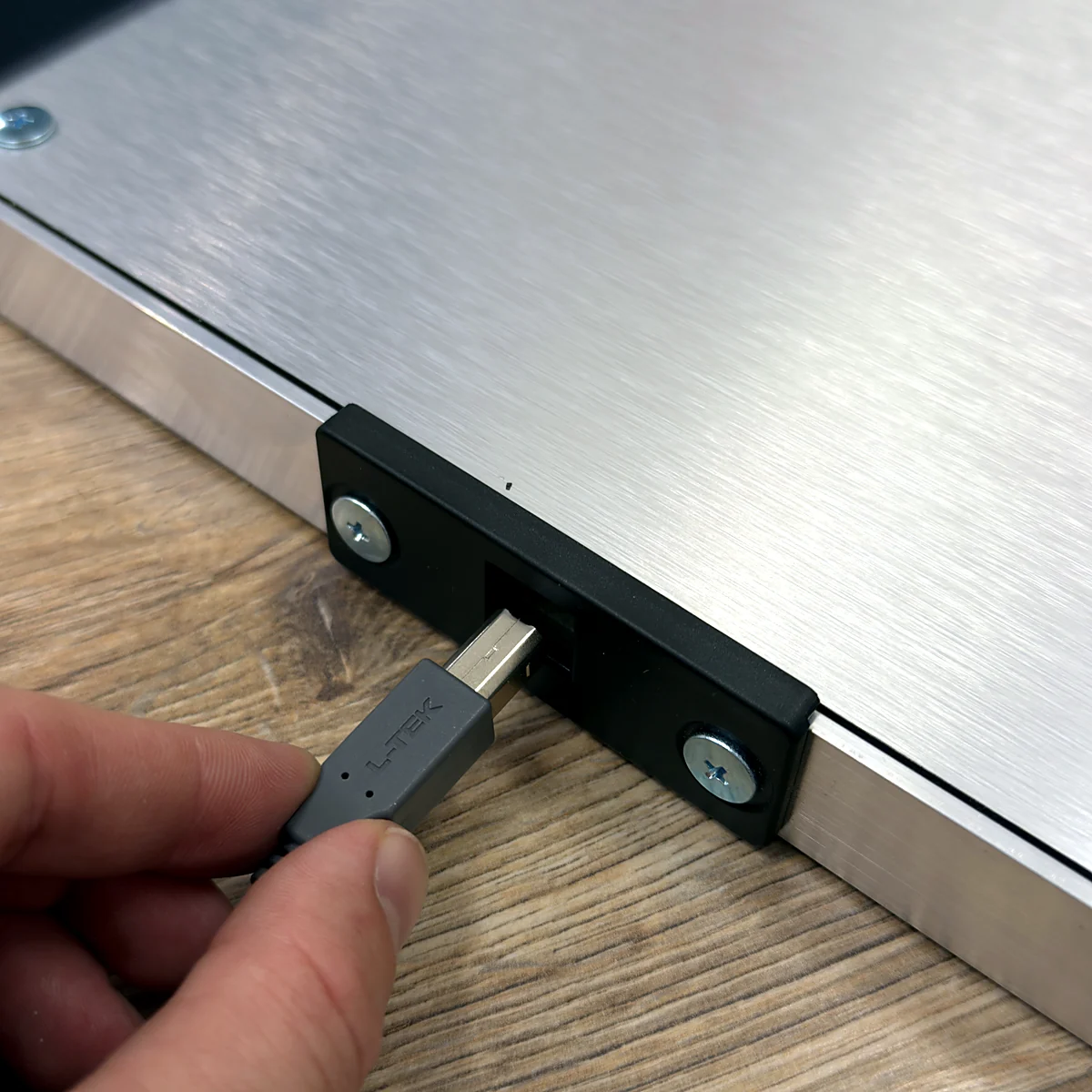 sq-piu-cable-connection - Interactive Mats L-TEK Hand plugging an L-TEK branded USB type-B cable into the connector block on the PIU PRO Metal frame